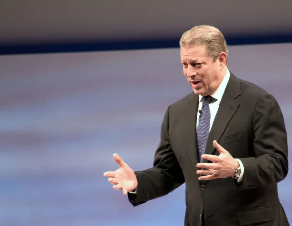 White man with graying dark hair in a suit holding his arms out in emphasis as he talks