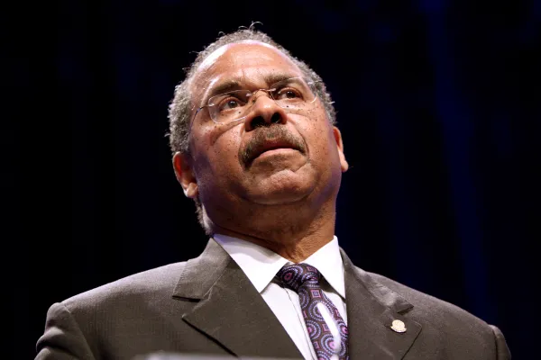 Black man in a suit with glasses speaking with his head tilted back