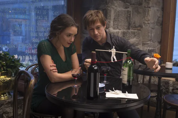 Man and woman sitting at a table looking at small replica of man on a wire between two towers