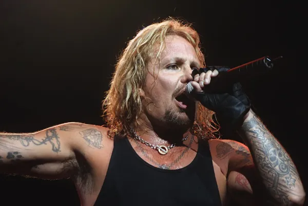 Vice Neil singing into mic with long stringy blonde hair and lots of tattoos